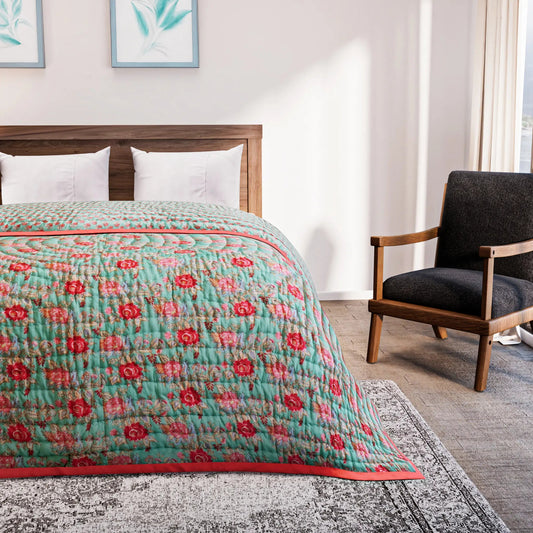 Bed with a floral quilt in a bedroom setting with a chair and artwork on the wall.