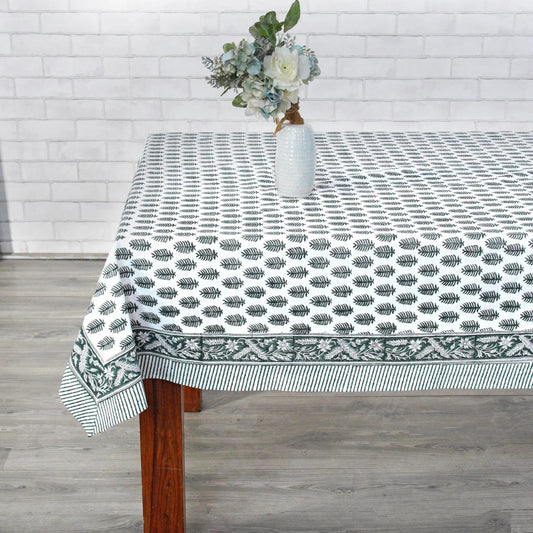 Tablecloth with leaf pattern on a wooden table against a white brick wall.