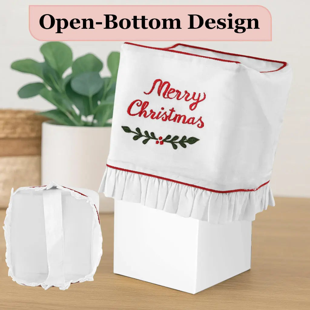 White kitchen towel with 'Merry Christmas' text and green leaves on a wooden surface with a plant in the background.