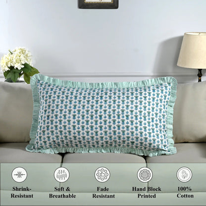 Cotton block print pillow cover placed on a bed with lamp and flowers in background.