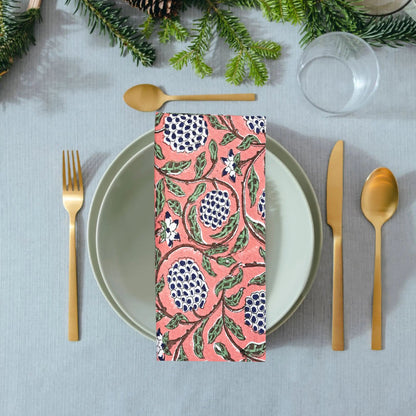 Table setting with a pink floral napkin, gold cutlery, and greenery on a gray tablecloth.