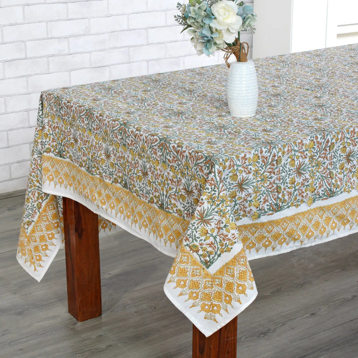 Tablecloth with floral pattern on a wooden table against a white brick wall.