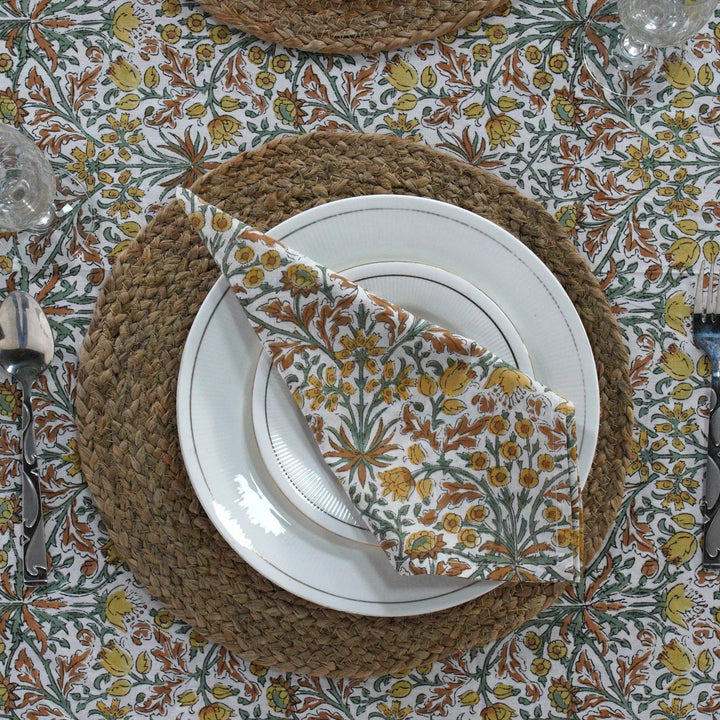Table setting with floral napkin, white plates, and woven placemat on a patterned tablecloth.