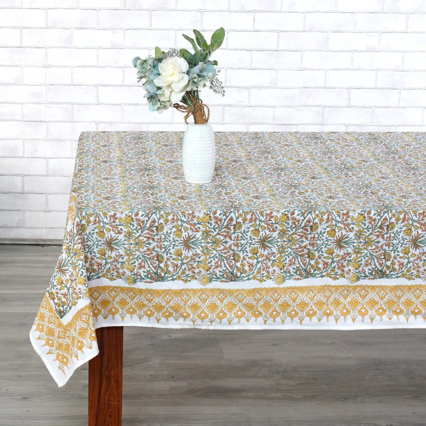 Tablecloth with floral pattern on a wooden table against a white brick wall.