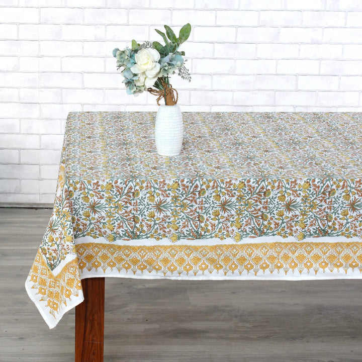 Tablecloth with floral pattern on a wooden table against a white brick wall.