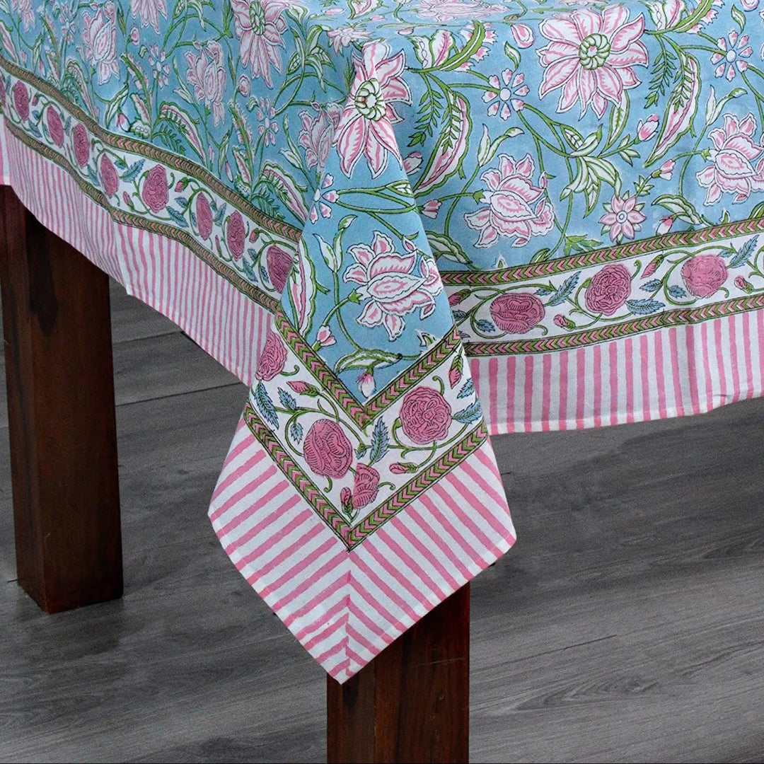 Tablecloth with floral pattern on a wooden table against a white brick wall.