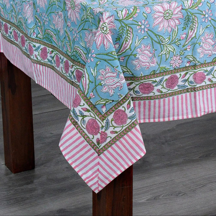 Tablecloth with floral pattern on a wooden table against a white brick wall.