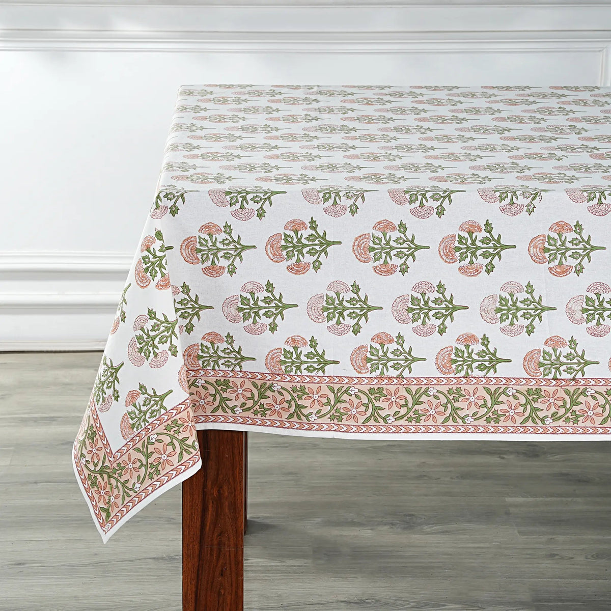 Tablecloth with floral pattern on a wooden table against a white wall.