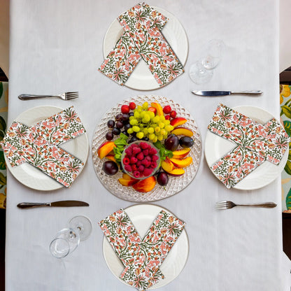 Table setting with floral napkins, fruit platter, and cutlery on a white tablecloth.
