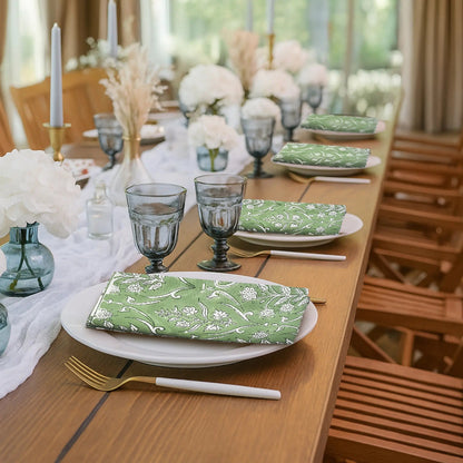 Dining table set with green patterned napkins, white flowers, and glassware in a bright room.
