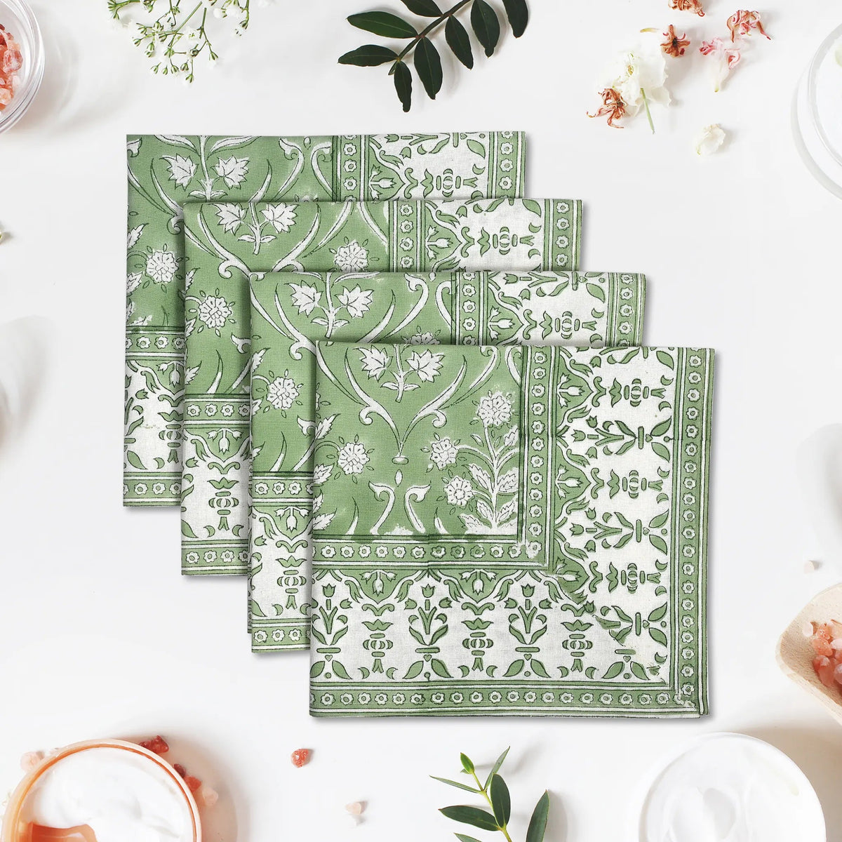 Set of green patterned napkins on a white surface with floral decorations.