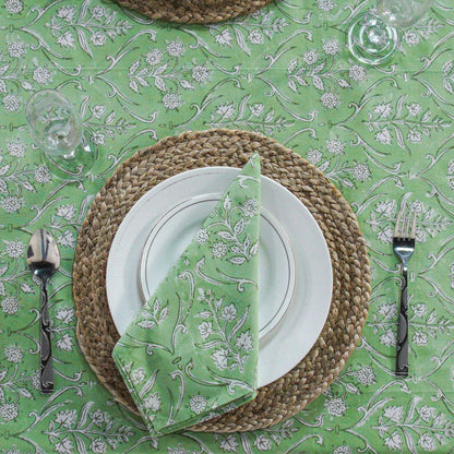 Dining table setting with green and white floral patterned tablecloth, plates, napkin, and cutlery.