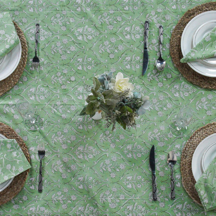 Green floral-patterned tablecloth with white plates, silverware, and woven placemats.