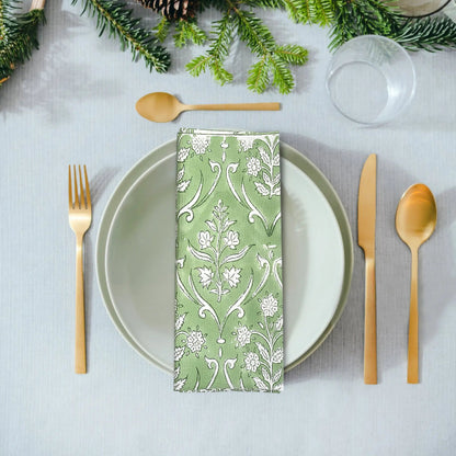 Table setting with a green patterned napkin, white plate, gold cutlery, and Christmas decorations.