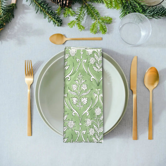 Table setting with a green patterned napkin, white plate, gold cutlery, and Christmas decorations.