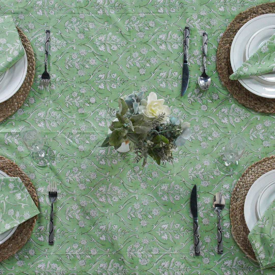Green floral-patterned tablecloth with white plates, silverware, and woven placemats.