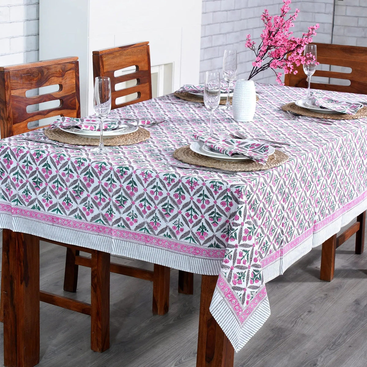 Dining table set with a patterned tablecloth, wooden chairs, and decorative elements.