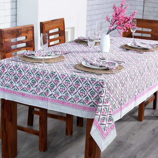 Dining table set with a patterned tablecloth, wooden chairs, and decorative elements.