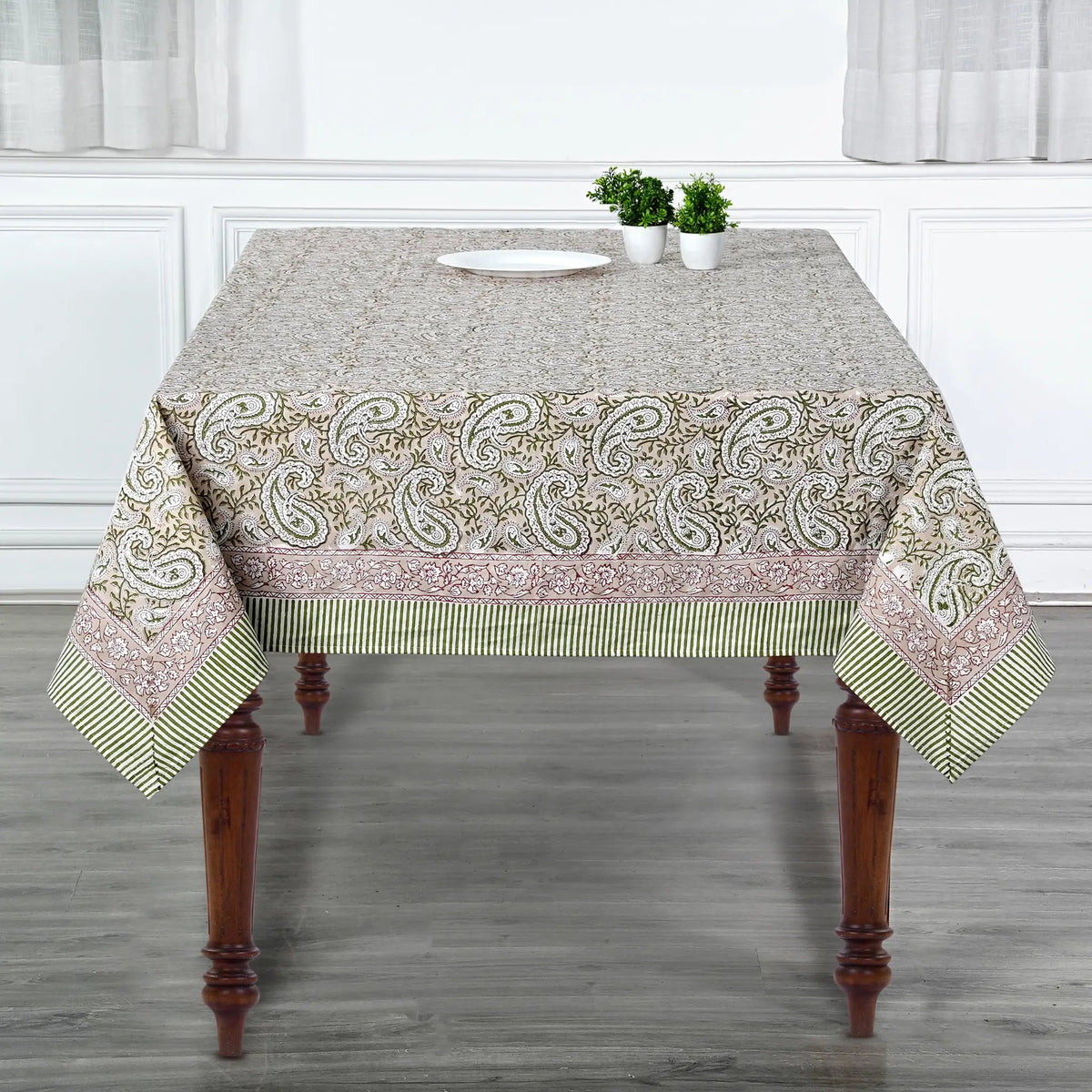 Tablecloth with paisley pattern on a wooden table in a room with white walls and gray floor.