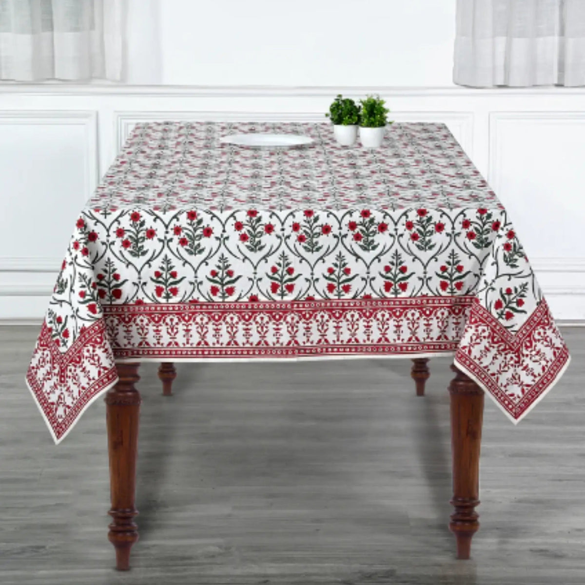 Tablecloth with floral pattern on a wooden table in a room with white curtains.