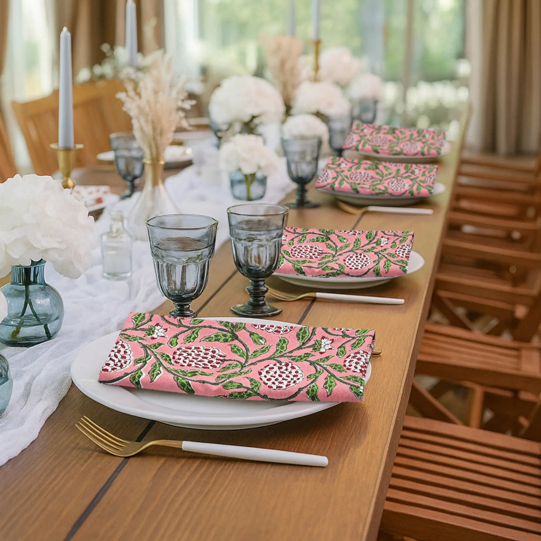 Dining table set with pink patterned napkins, glasses, and cutlery in a bright room.