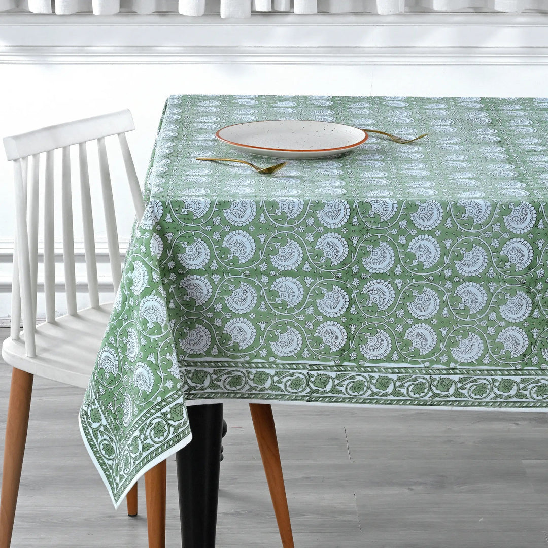 Green patterned tablecloth on a dining table with a chair in a kitchen setting.