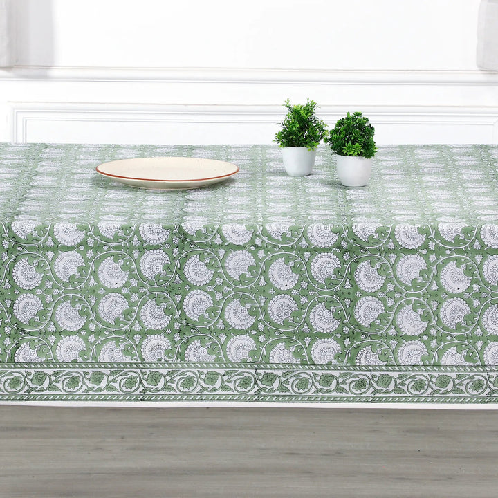 Green and white patterned tablecloth on a wooden table with plants and a plate.