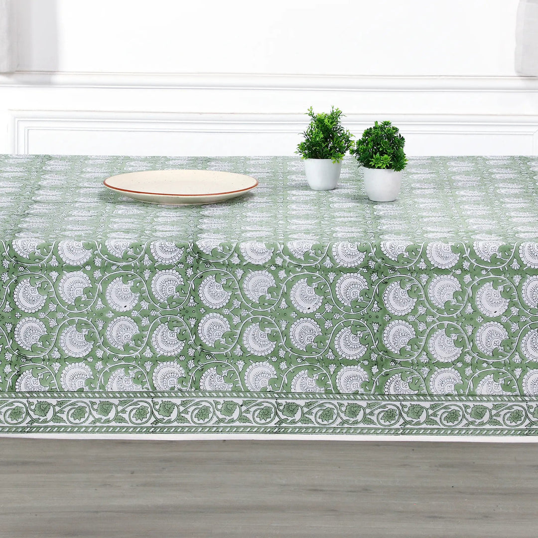 Green and white patterned tablecloth on a wooden table with plants and a plate.