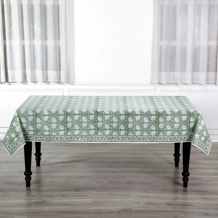 Tablecloth with green floral pattern on a wooden table in a room with white curtains.