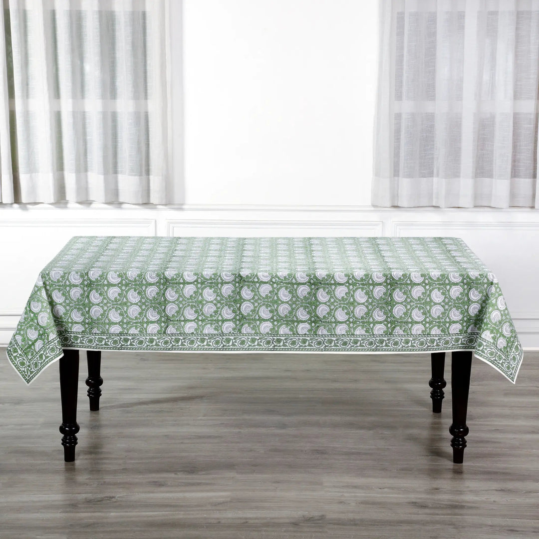 Tablecloth with green floral pattern on a wooden table in a room with white curtains.