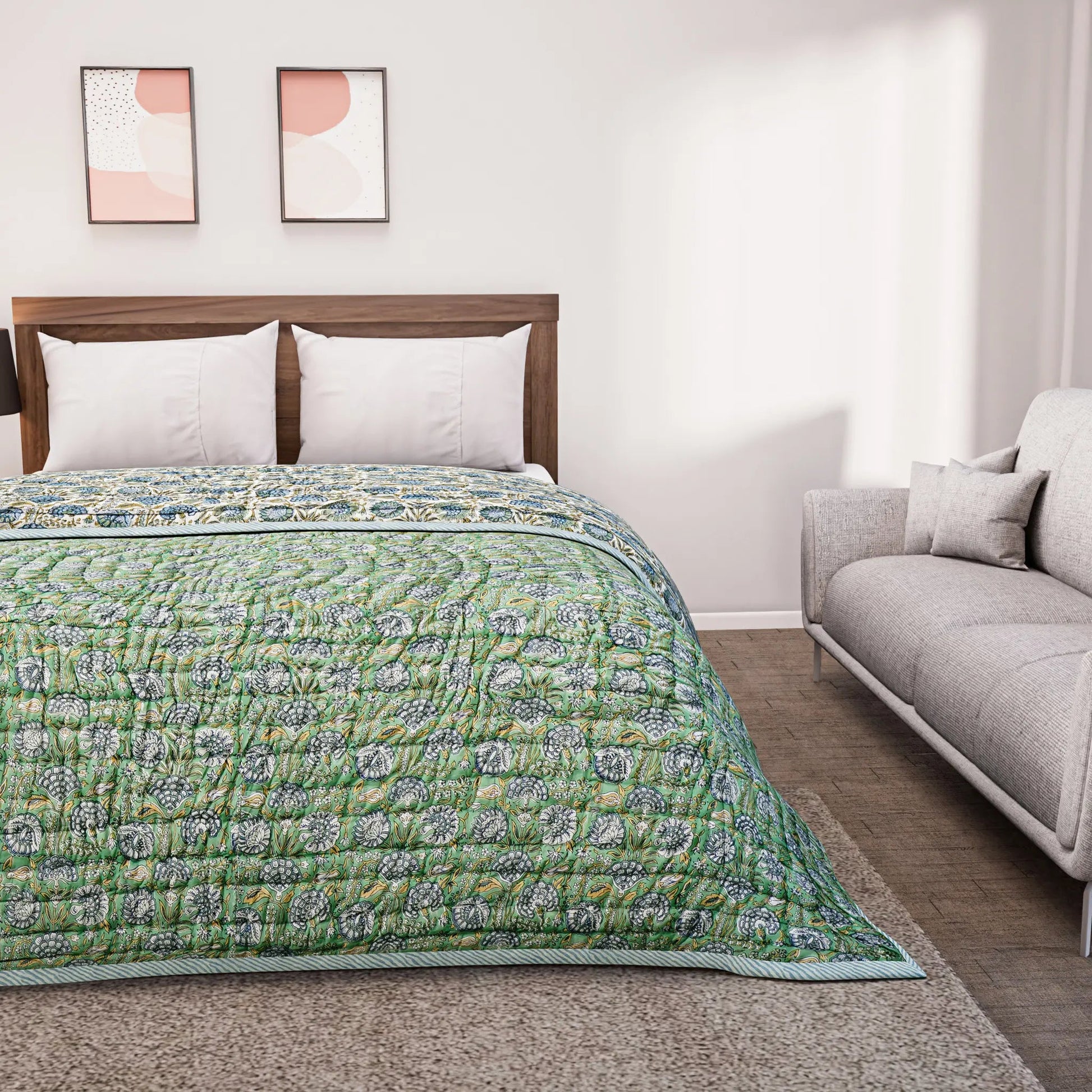 Bed with green floral quilt and white pillows in a room with a gray sofa and abstract wall art.