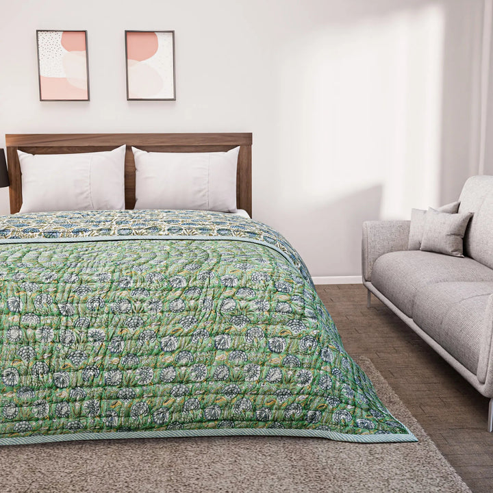 Bed with green floral quilt and white pillows in a room with a gray sofa and abstract wall art.