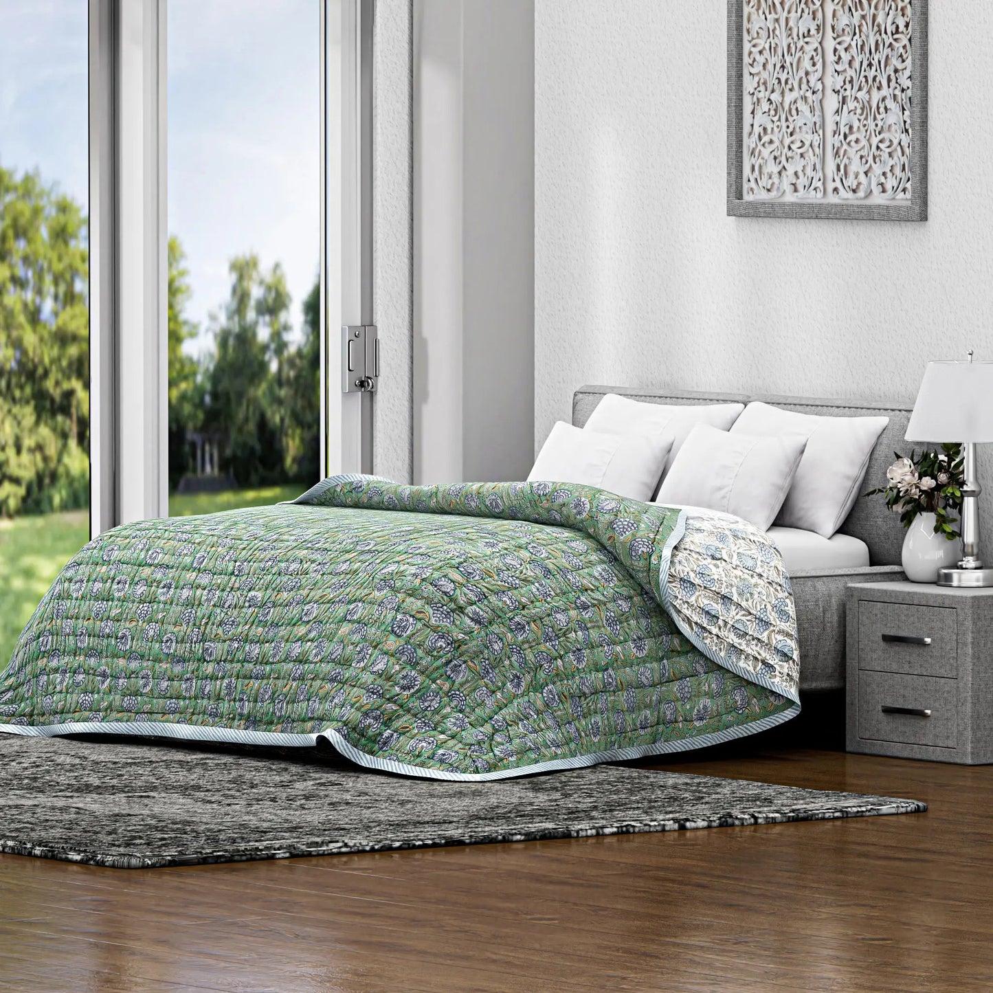 Bed with green quilt in a bright bedroom with large windows.