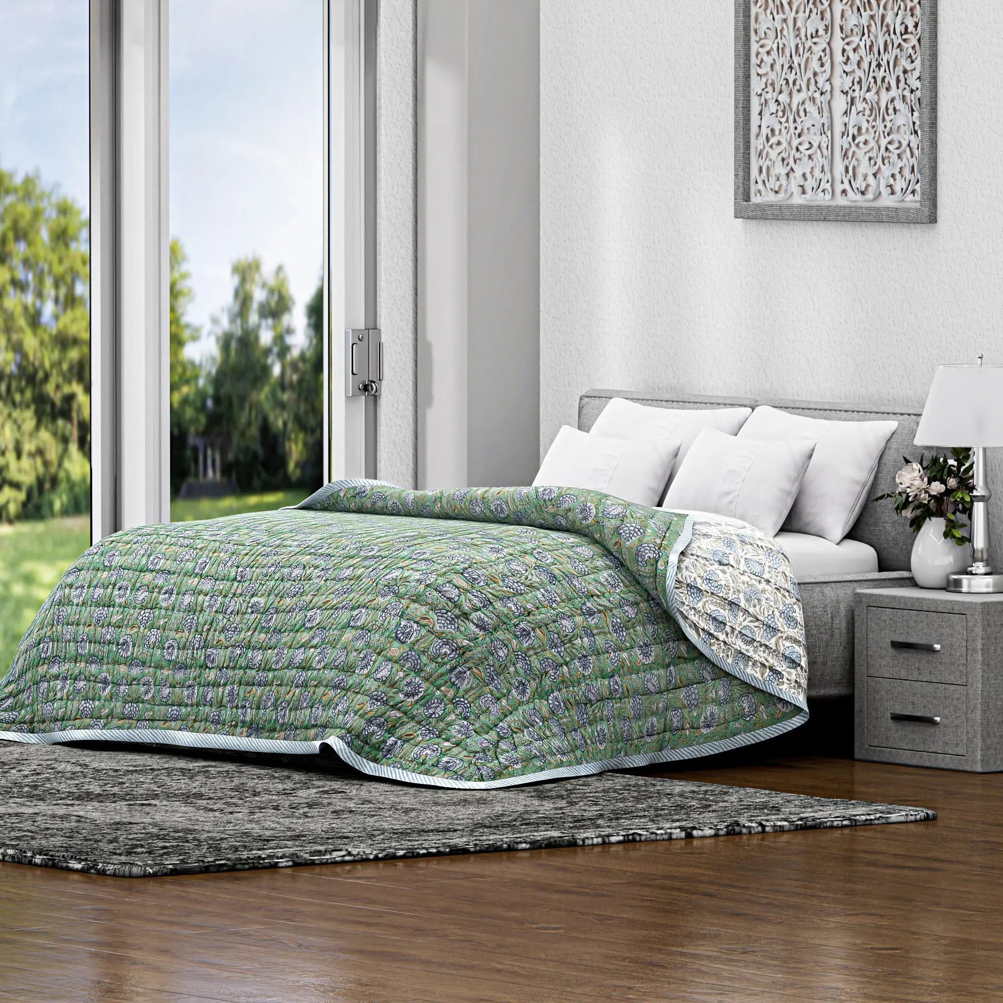 Bed with green quilt in a bright bedroom with large windows.