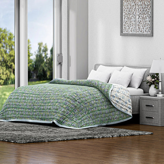 Bed with green quilt in a bright bedroom with large windows.