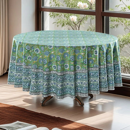 Round table with a green floral patterned tablecloth in a bright room with windows.