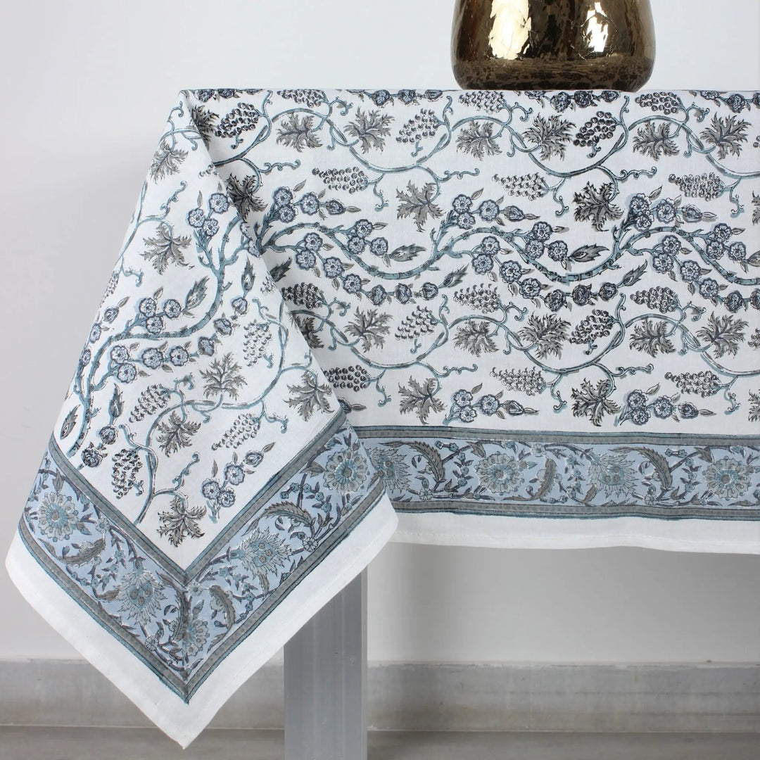 Tablecloth with floral pattern on a table, accompanied by a vase of pink flowers.
