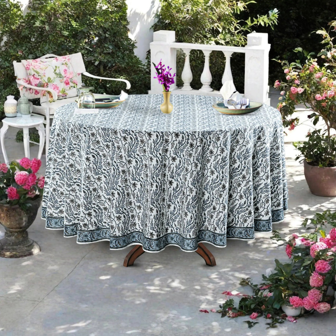 Outdoor table setting with a patterned tablecloth, chairs, and floral arrangements.