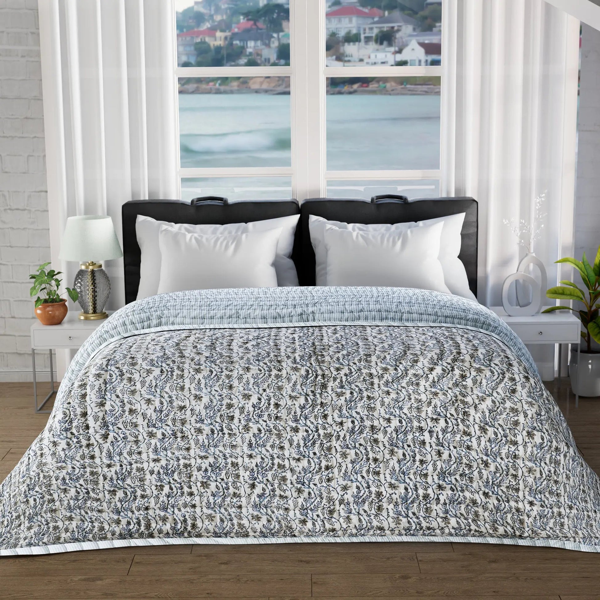 Bed with patterned quilt and white pillows in a room with large windows showing a scenic view.