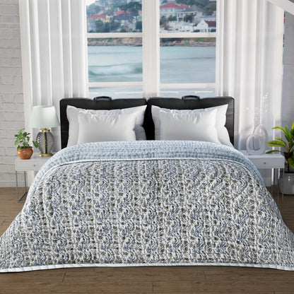 Bed with patterned quilt and white pillows in a room with large windows showing a scenic view.
