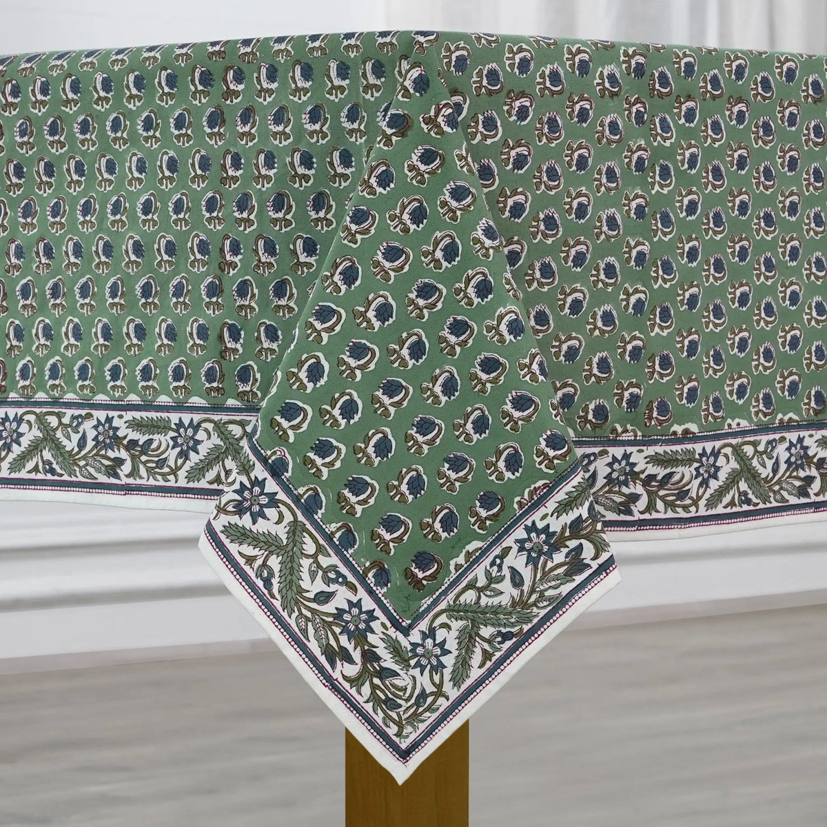 Green patterned tablecloth on a wooden table with a white curtain background