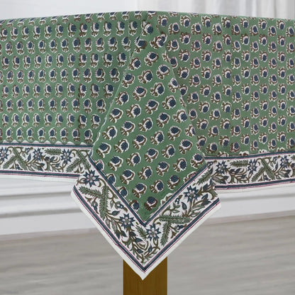 Green patterned tablecloth on a wooden table with a white curtain background