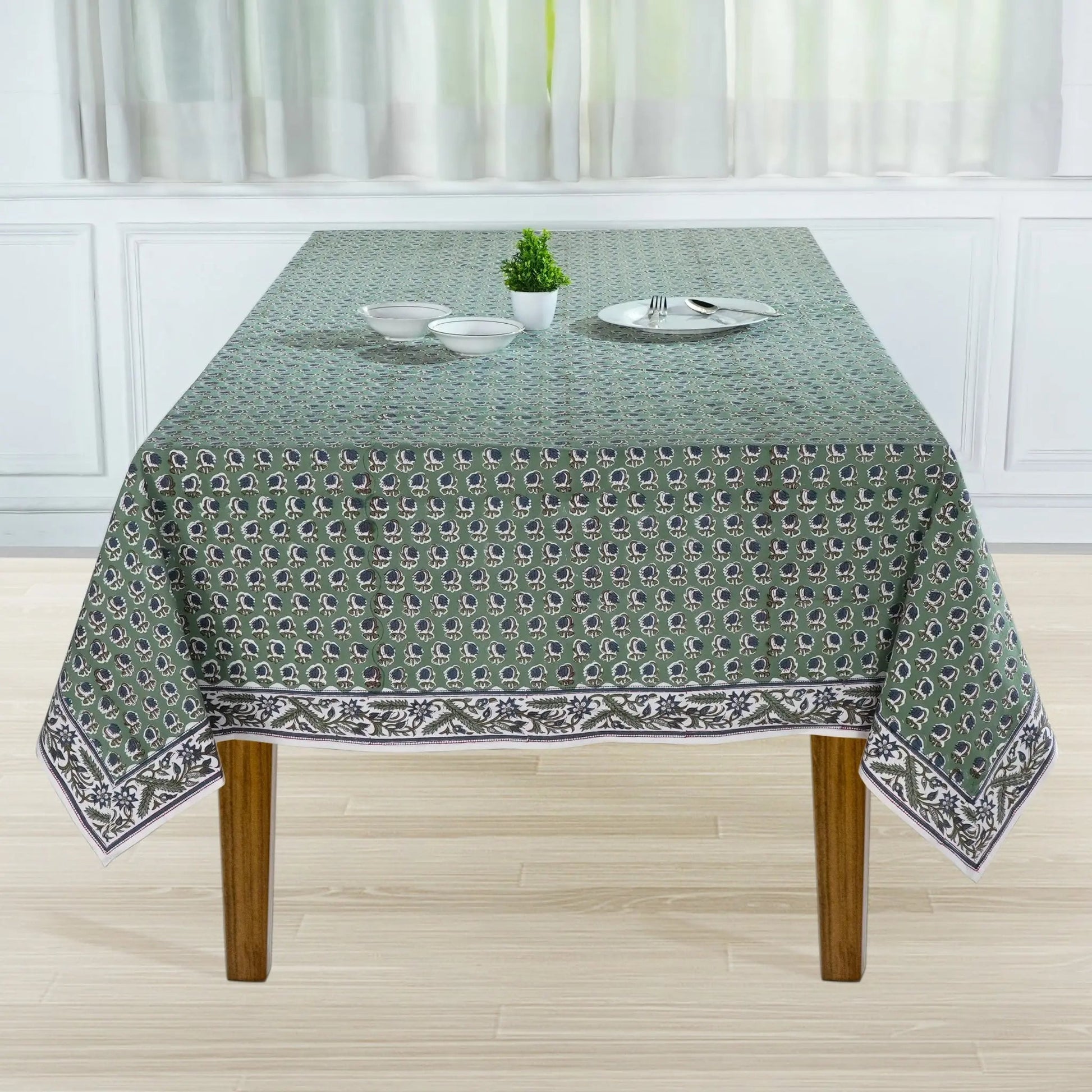 Tablecloth with a pattern on a wooden table in a room with white curtains.