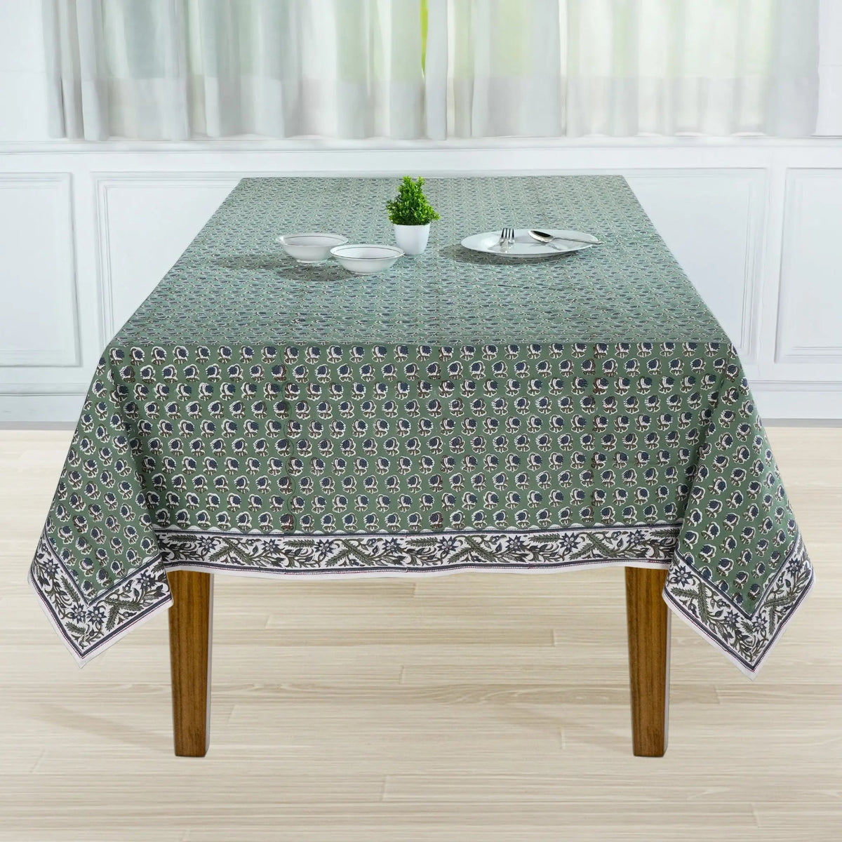 Tablecloth with a pattern on a wooden table in a room with white curtains.