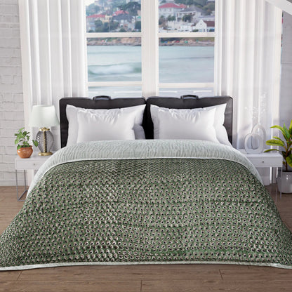 Bed with green patterned comforter in a room with large windows showing a waterfront view.