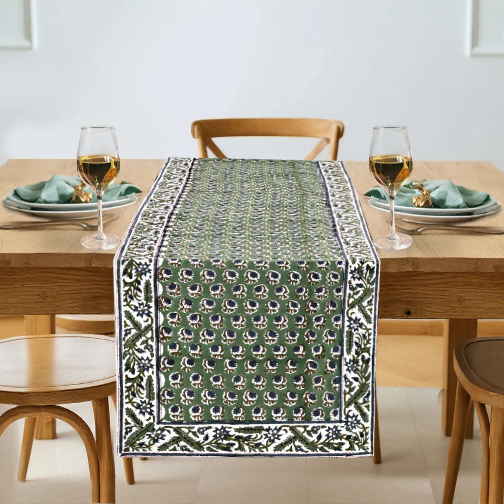 Dining table set with a green patterned table runner, glasses, and plates.