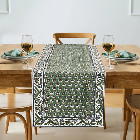 Dining table set with a green patterned table runner, glasses, and plates.