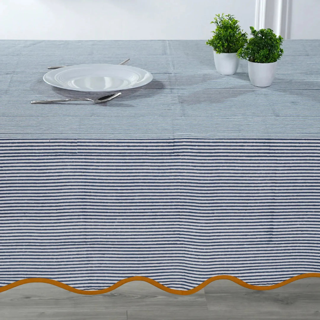 Tablecloth with blue and white stripes and gold border on a table setting.