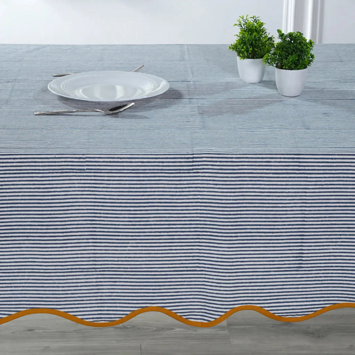 Tablecloth with blue and white stripes and gold border on a table setting.