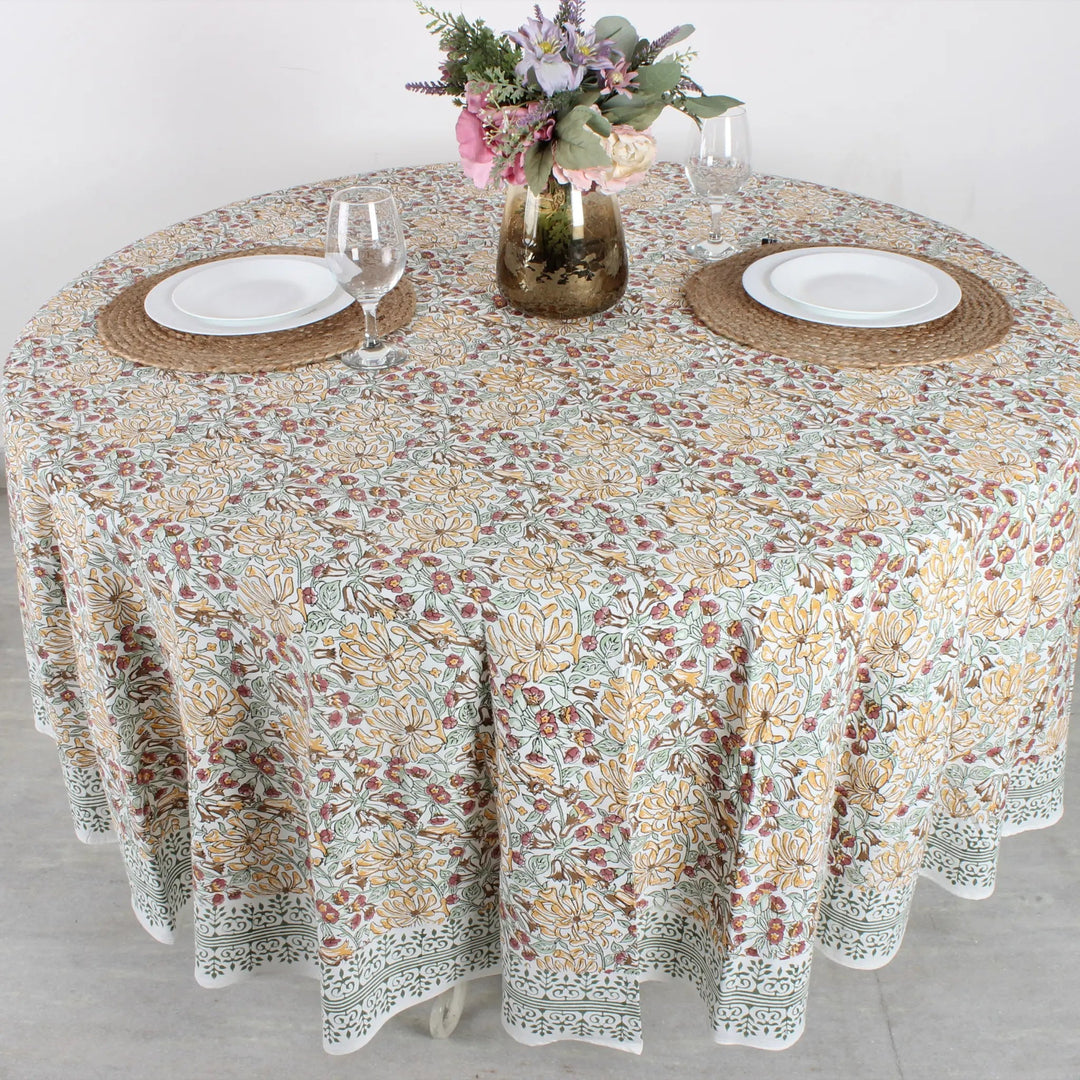 Round table with floral patterned tablecloth, plates, and glasses on a light background